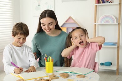 Photo of Speech therapist teaching little kids alphabet at white table indoors