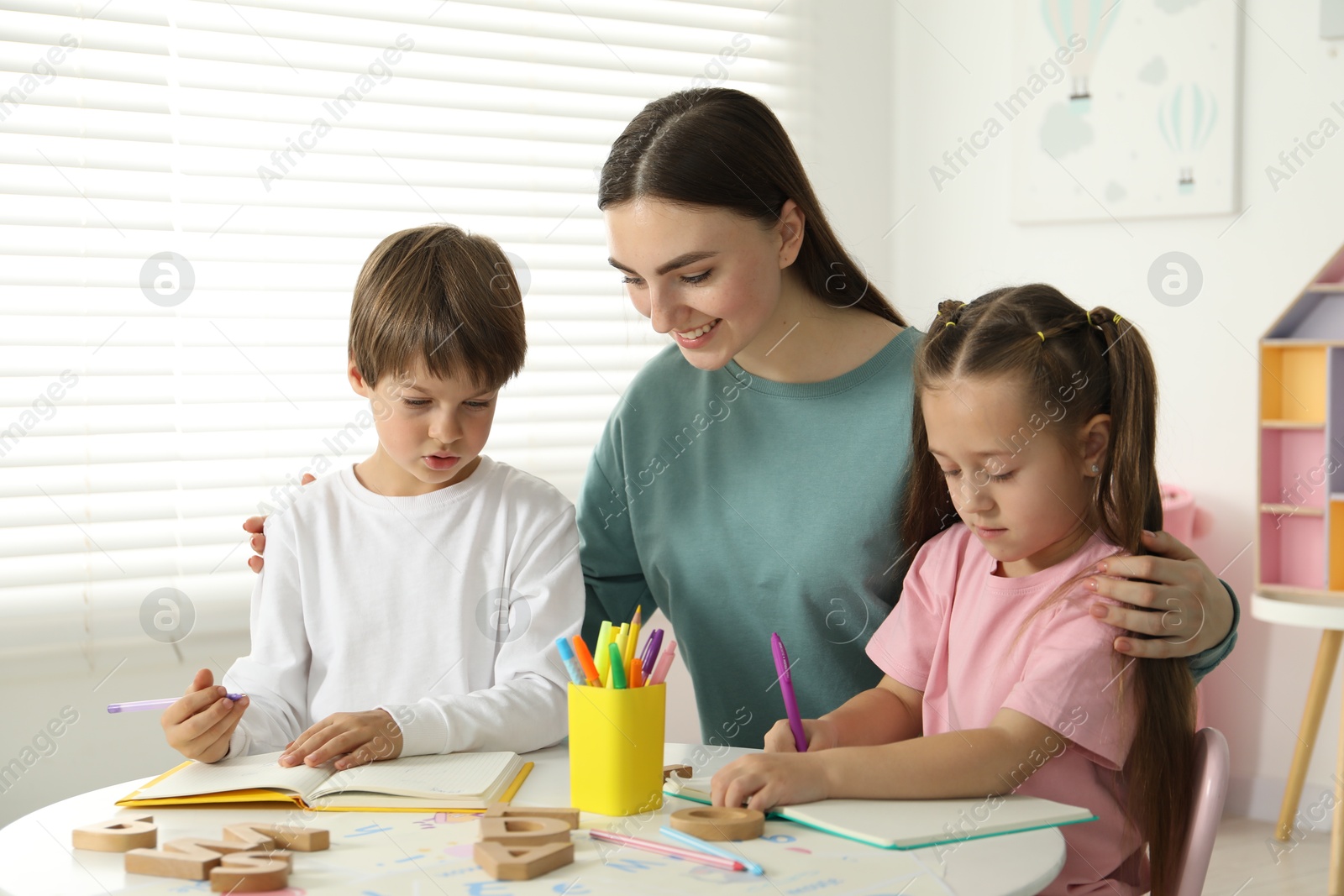 Photo of Speech therapist teaching little kids alphabet at white table indoors