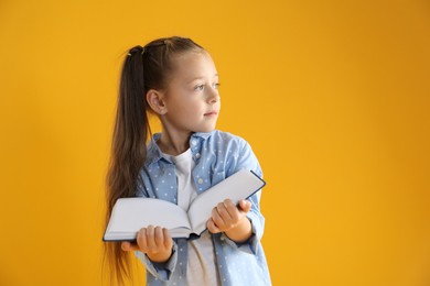 Photo of Learning alphabet. Little girl with book on orange background, space for text