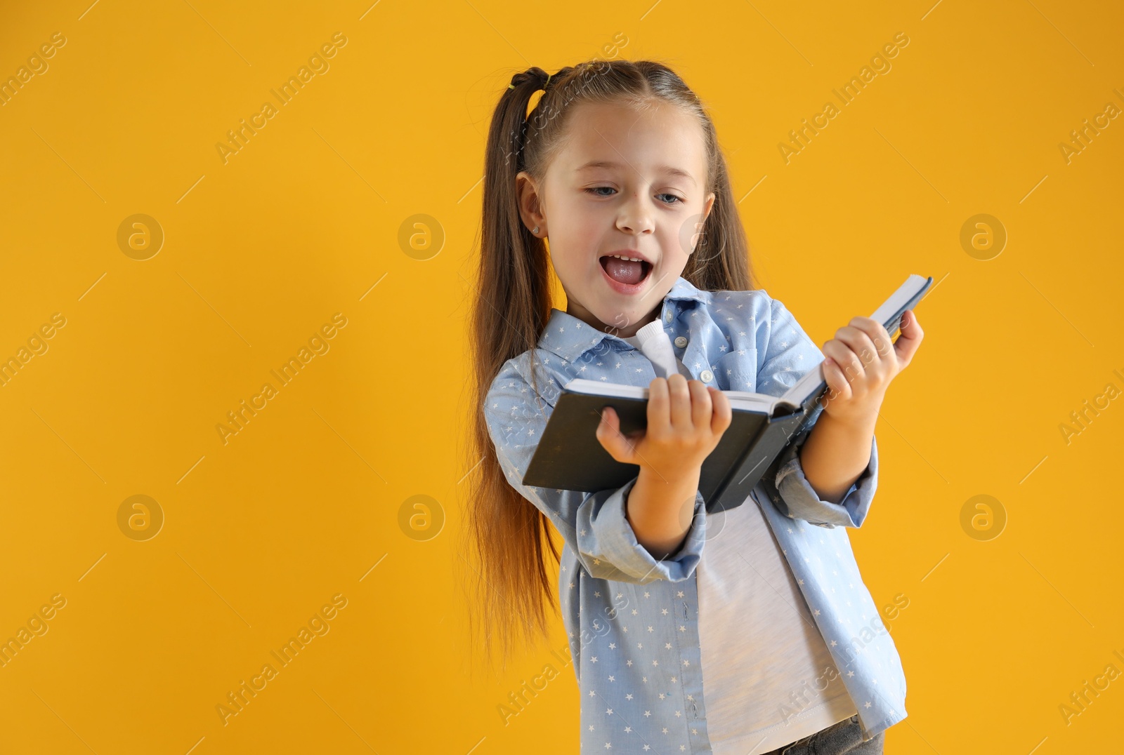 Photo of Learning alphabet. Little girl with book on orange background, space for text