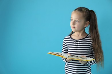 Photo of Learning alphabet. Little girl with book on light blue background, space for text