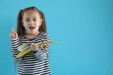 Photo of Learning alphabet. Little girl with book on light blue background, space for text