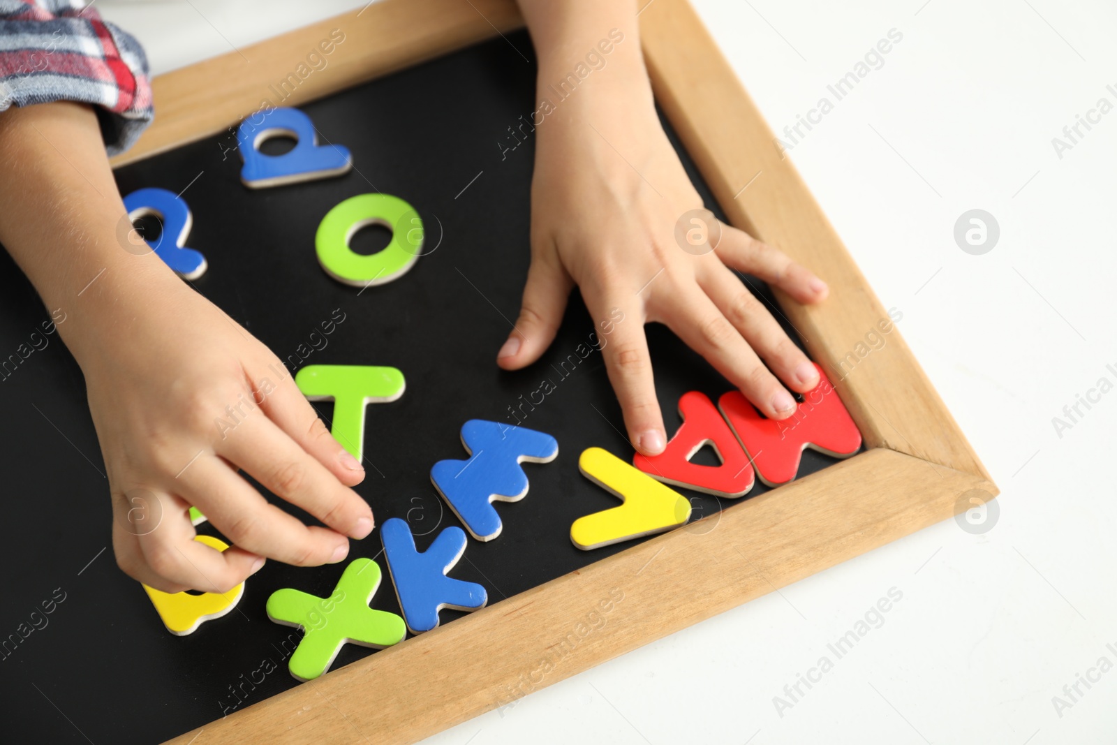 Photo of Little boy learning alphabet with magnetic letters at white table indoors, closeup