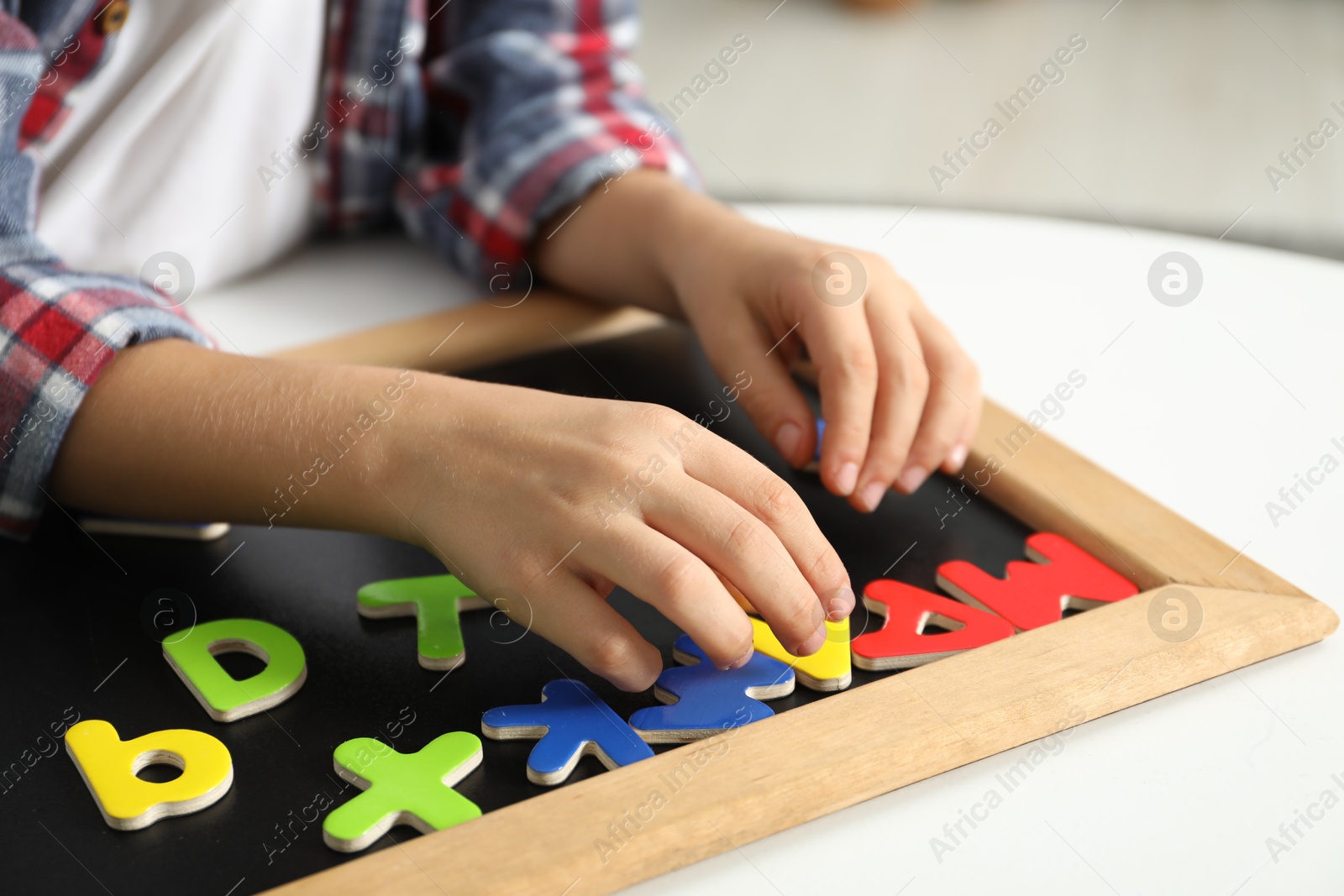 Photo of Little boy learning alphabet with magnetic letters at white table indoors, closeup