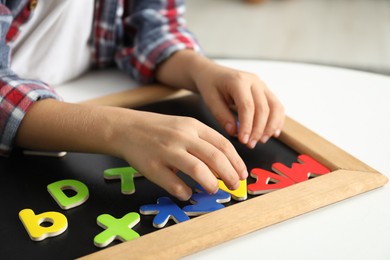 Photo of Little boy learning alphabet with magnetic letters at white table indoors, closeup