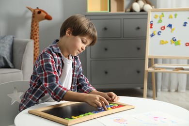 Little boy learning alphabet with magnetic letters at white table indoors