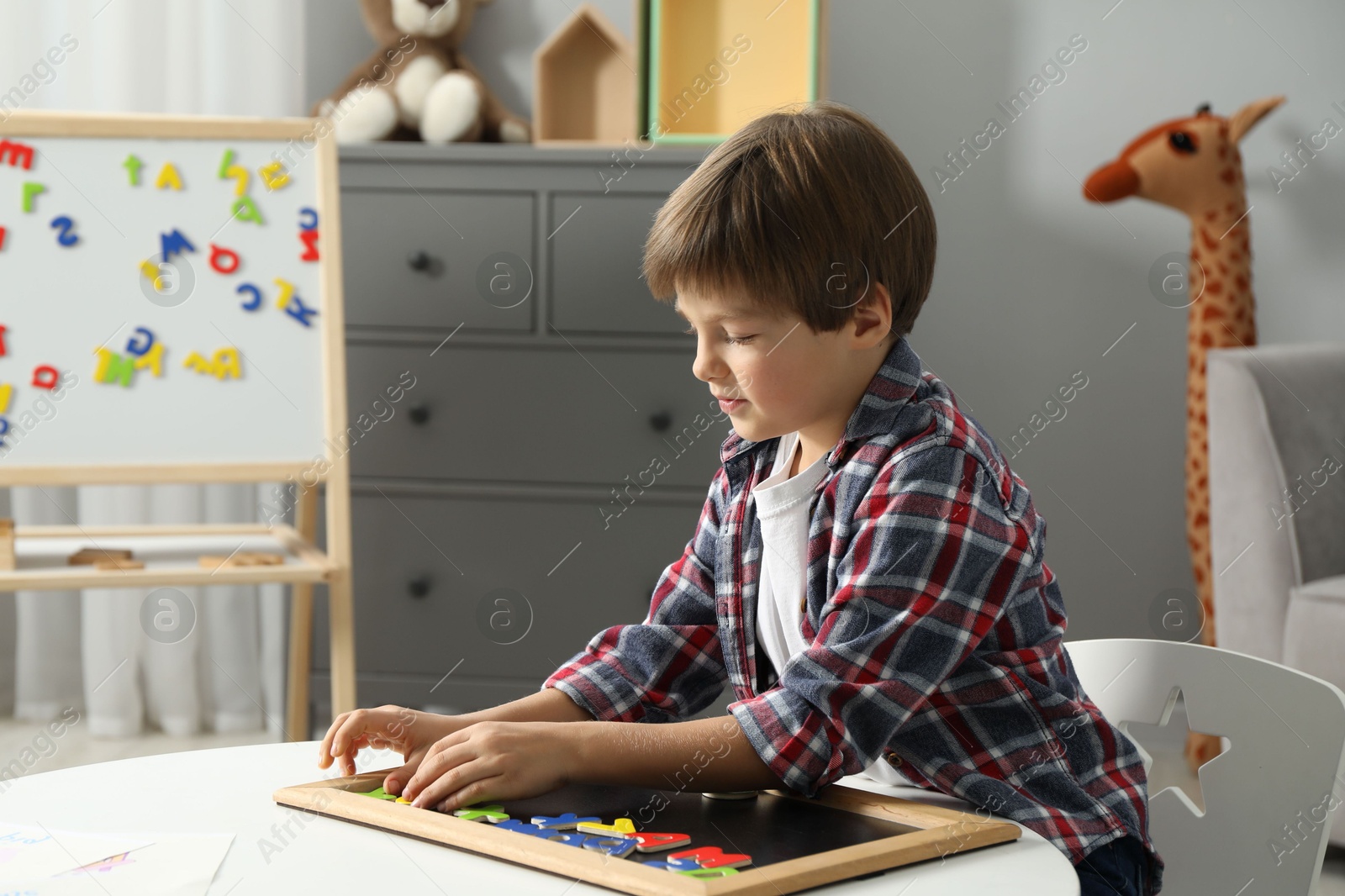 Photo of Little boy learning alphabet with magnetic letters at white table indoors