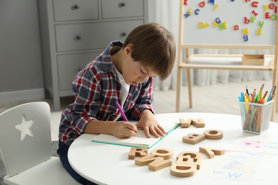 Photo of Little boy learning alphabet at white table indoors