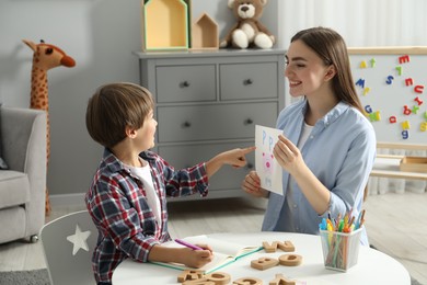 Speech therapist teaching little boy alphabet at white table indoors