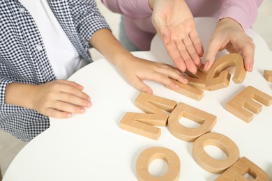 Speech therapist teaching little boy alphabet with wooden letters at white table indoors, closeup