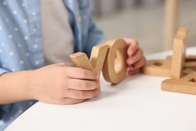 Photo of Little girl learning alphabet with wooden letters at white table indoors, closeup