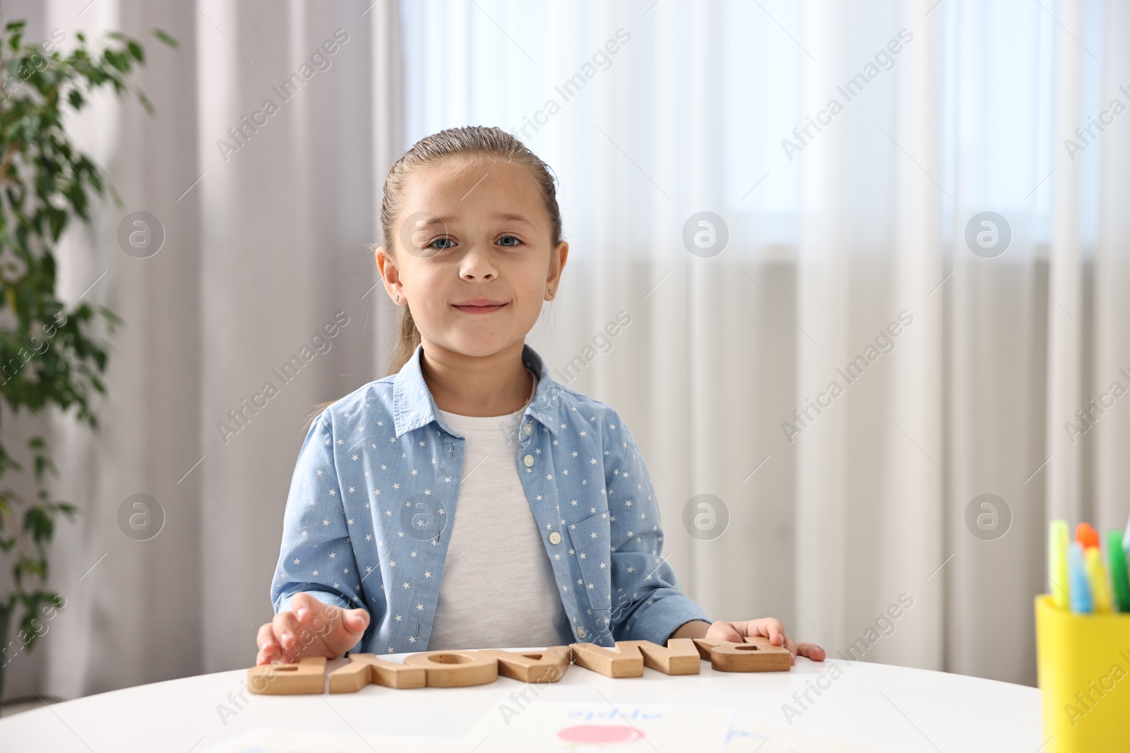 Photo of Little girl learning alphabet with wooden letters at white table indoors