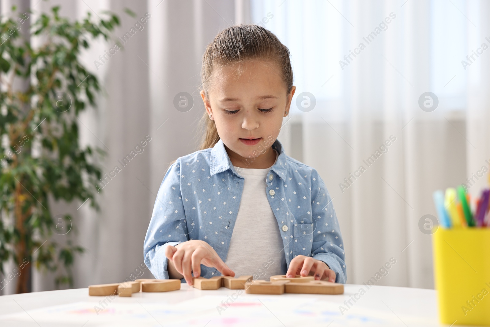 Photo of Little girl learning alphabet with wooden letters at white table indoors