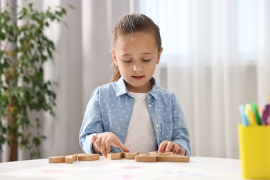 Photo of Little girl learning alphabet with wooden letters at white table indoors