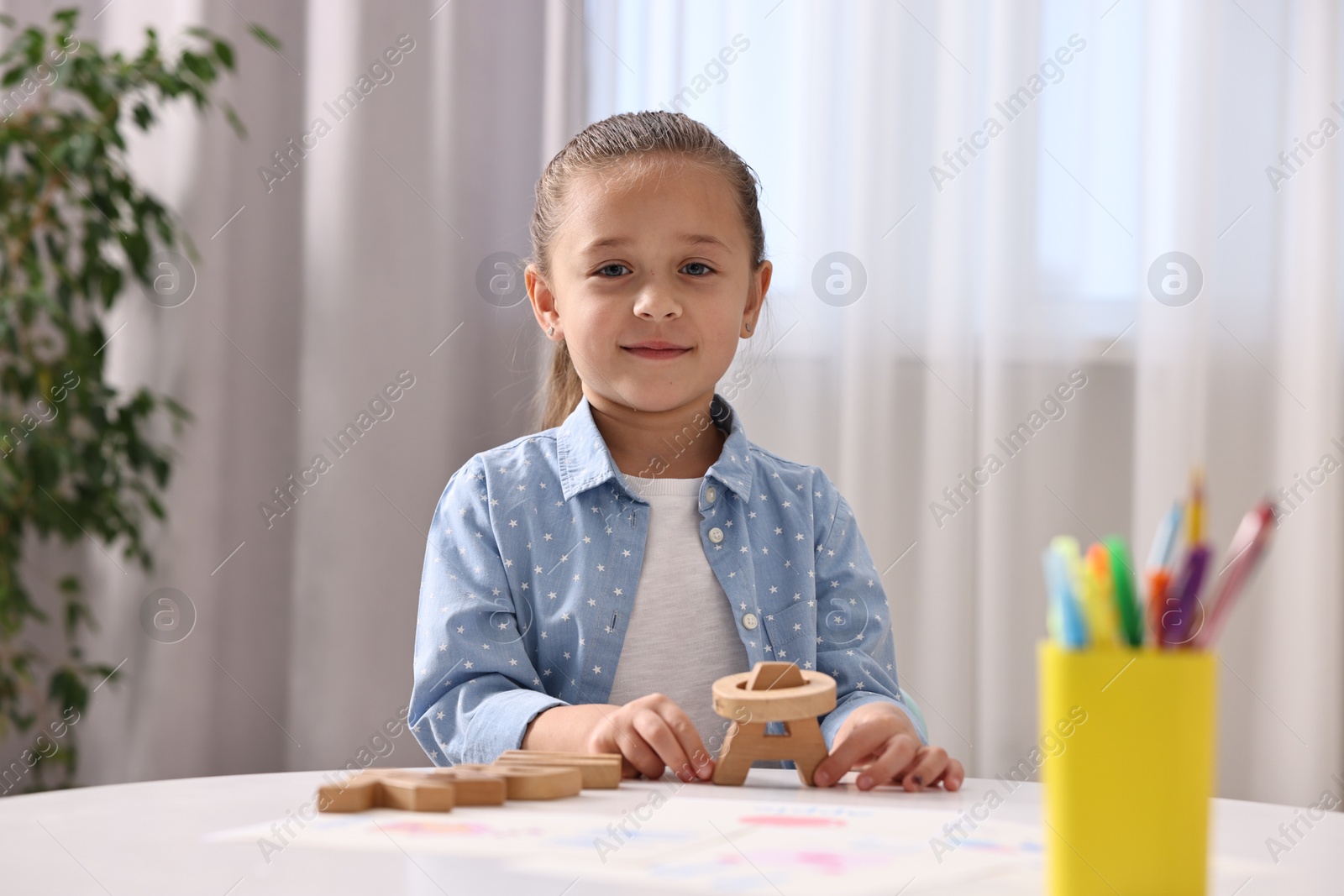 Photo of Little girl learning alphabet with wooden letters at white table indoors