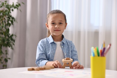 Little girl learning alphabet with wooden letters at white table indoors