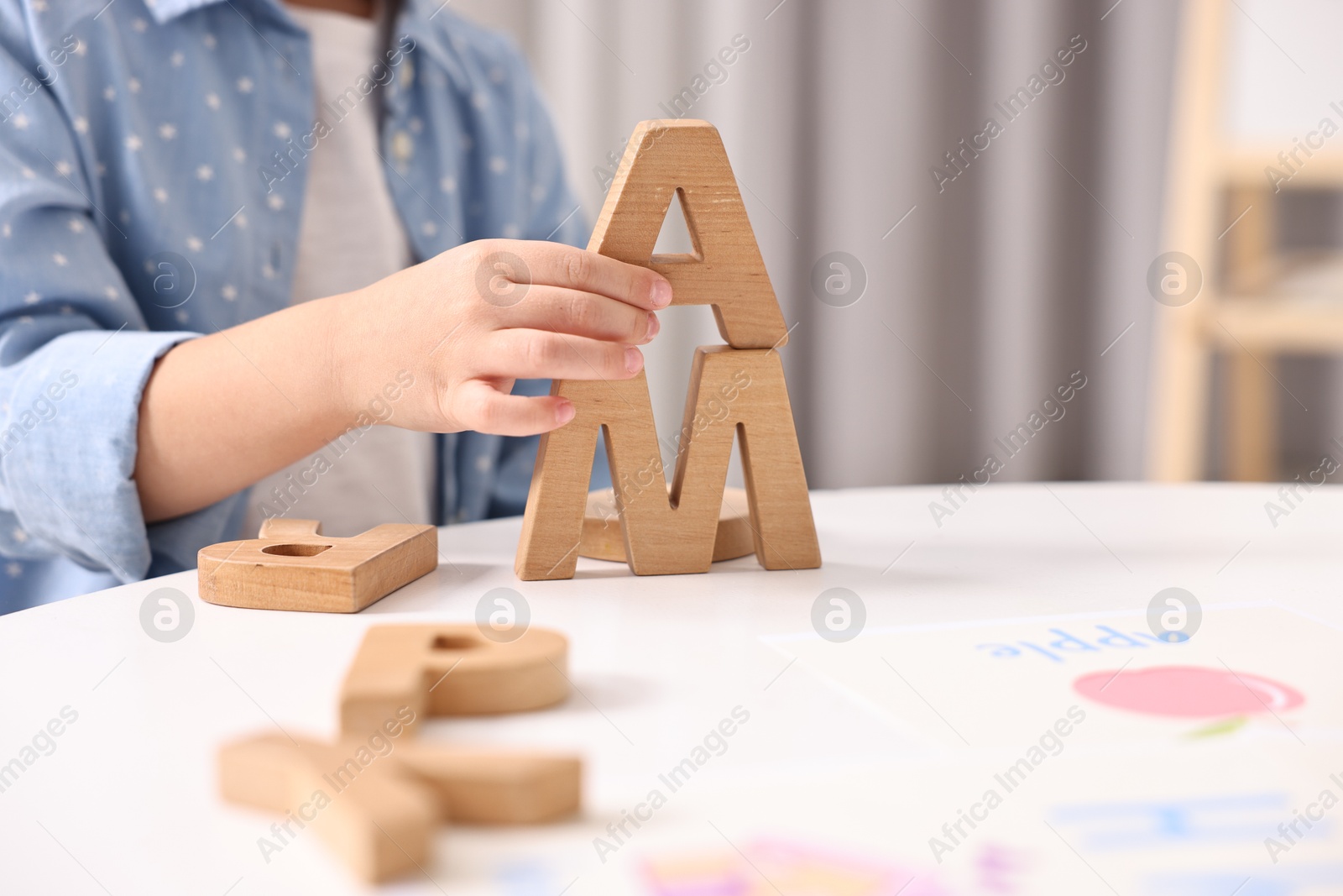 Photo of Little girl learning alphabet with wooden letters at white table indoors, closeup