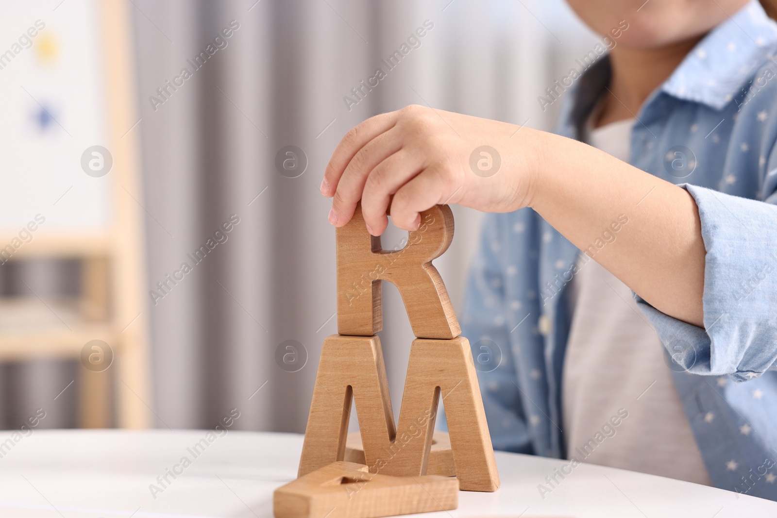 Photo of Little girl learning alphabet with wooden letters at white table indoors, closeup. Space for text