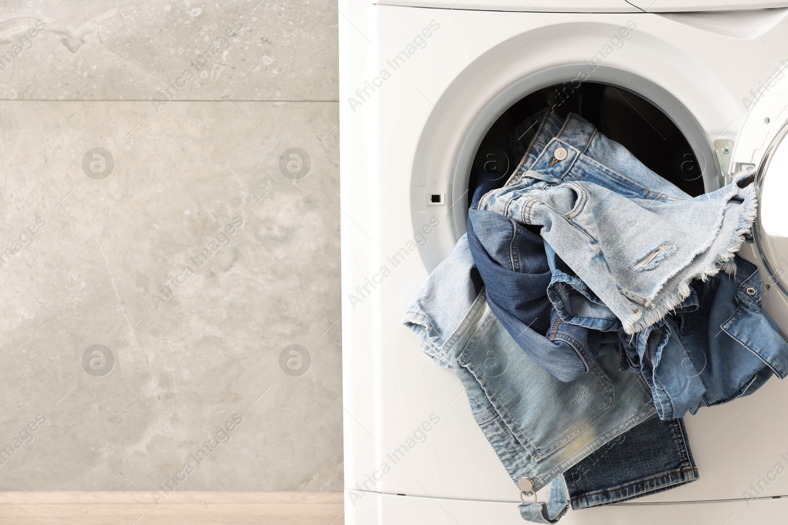 Photo of Washing machine with dirty jeans and other denim clothes indoors, space for text