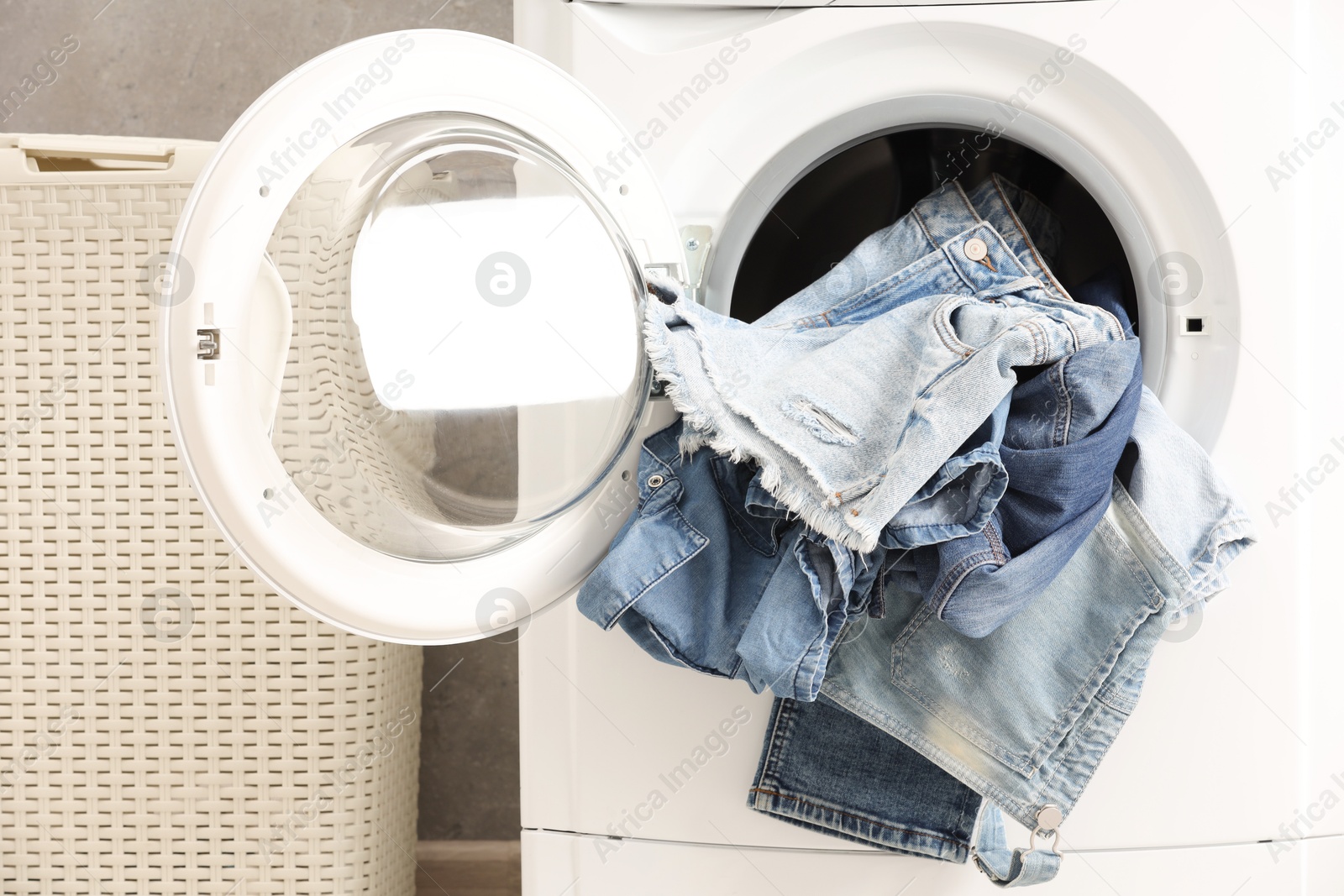 Photo of Washing machine with dirty jeans and other denim clothes indoors