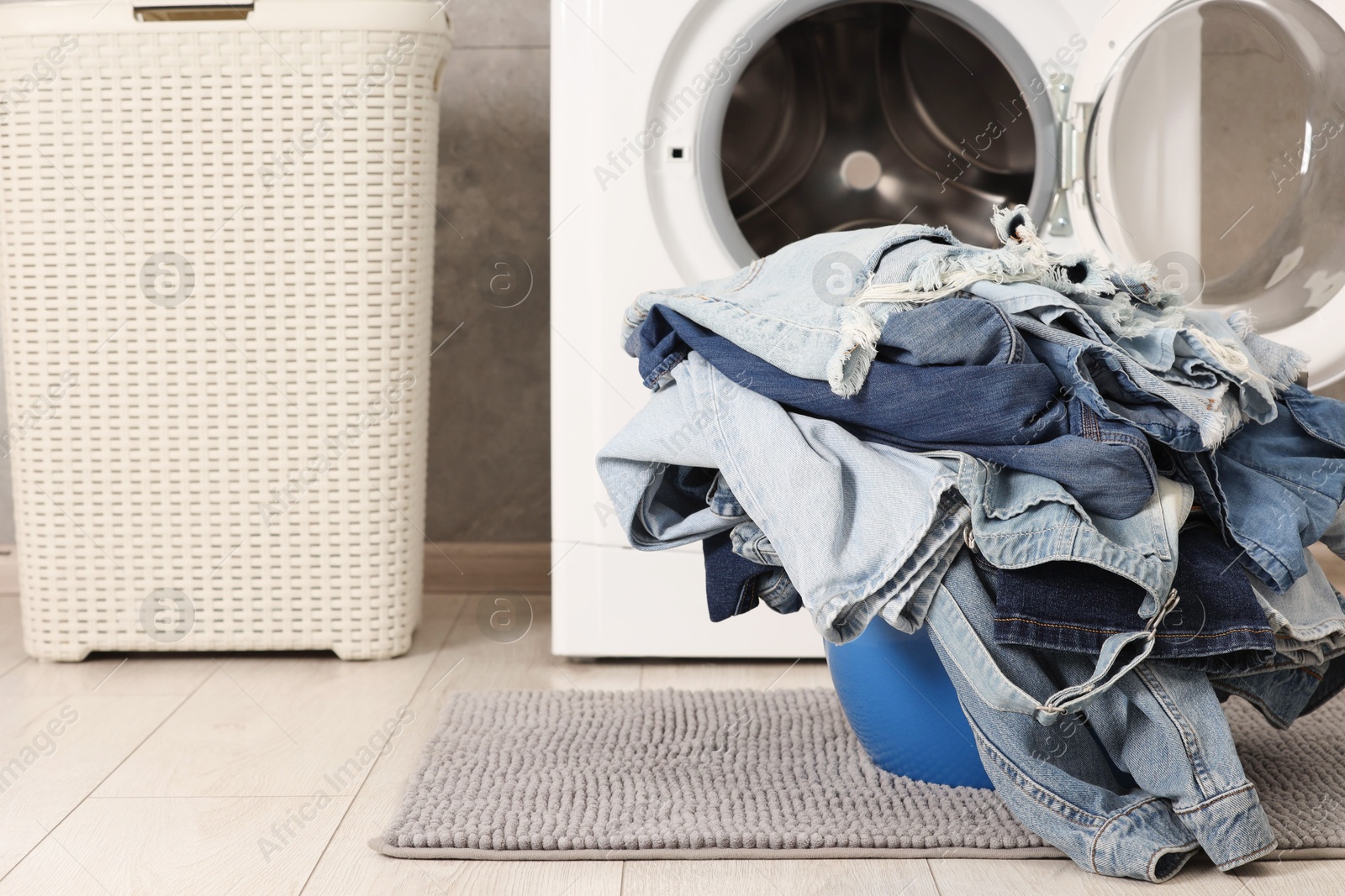 Photo of Washing machine and laundry basket with dirty denim clothes indoors, space for text