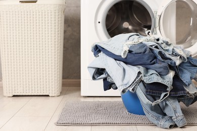 Photo of Washing machine and laundry basket with dirty denim clothes indoors, space for text