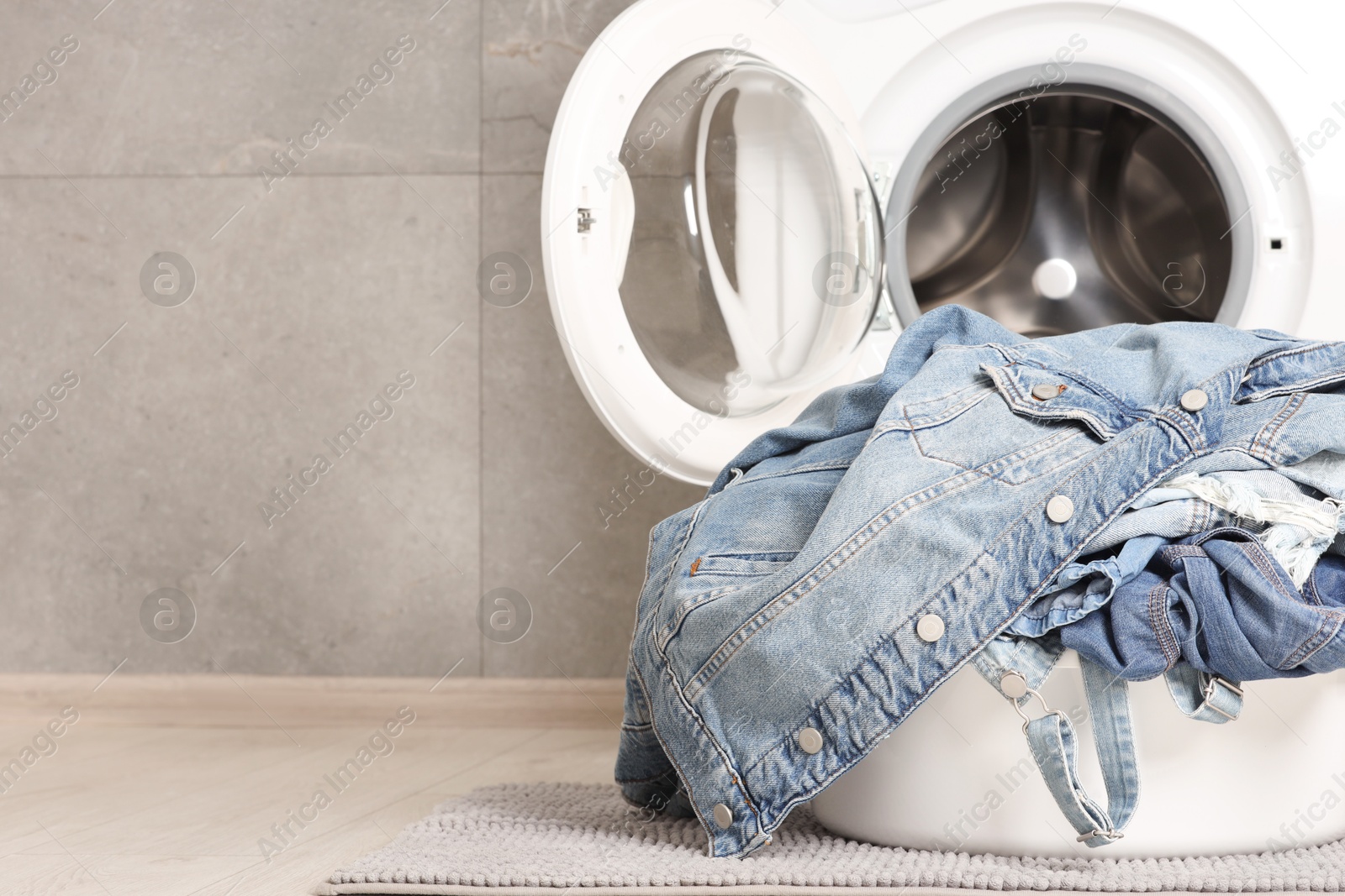 Photo of Washing machine and laundry basket with dirty denim clothes indoors, space for text