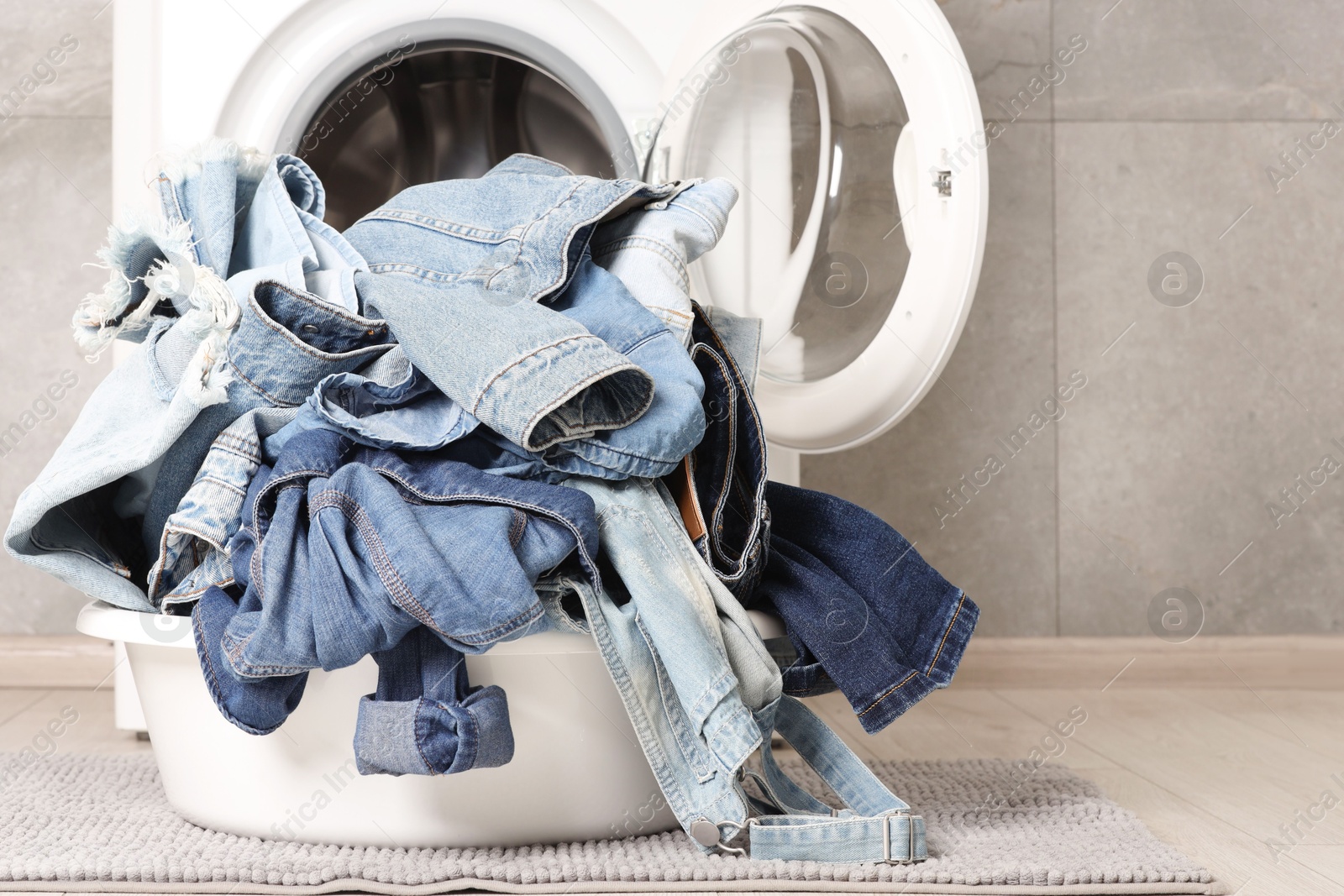 Photo of Washing machine and laundry basket with dirty denim clothes indoors