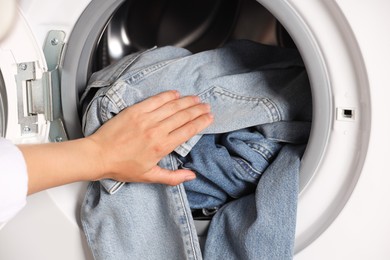 Woman putting dirty jeans and other denim clothes into washing machine, closeup