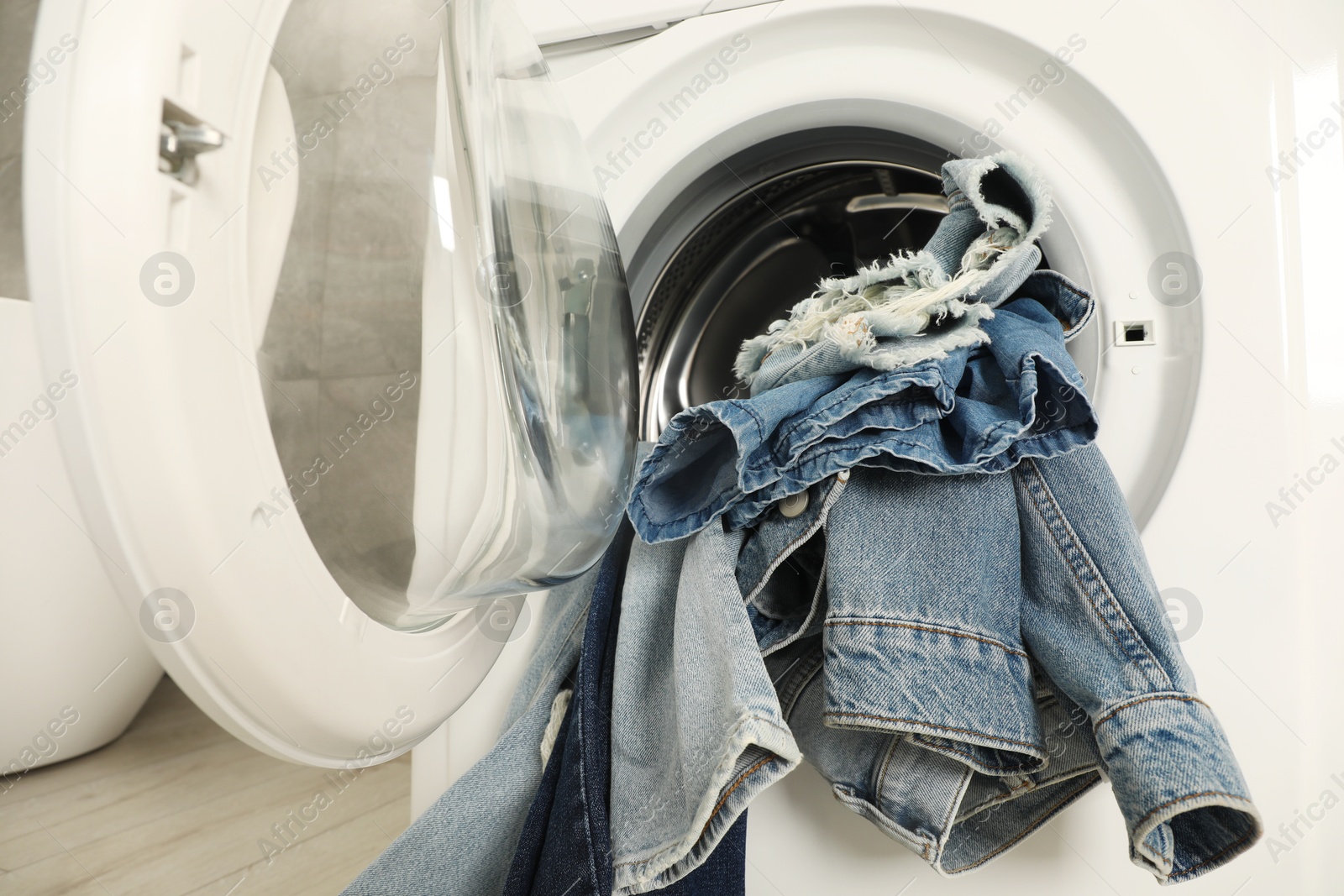 Photo of Washing machine with dirty jeans and other denim clothes indoors