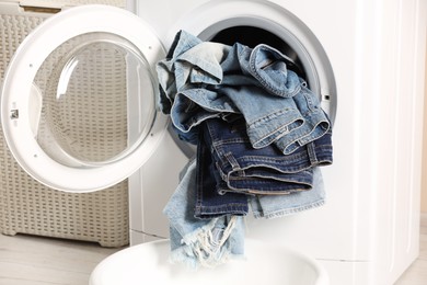 Photo of Washing machine with dirty jeans and other denim clothes indoors