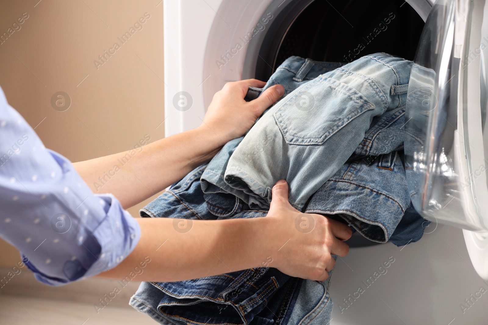 Photo of Woman putting dirty jeans and other denim clothes into washing machine, closeup