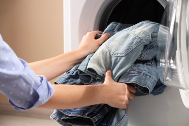 Woman putting dirty jeans and other denim clothes into washing machine, closeup