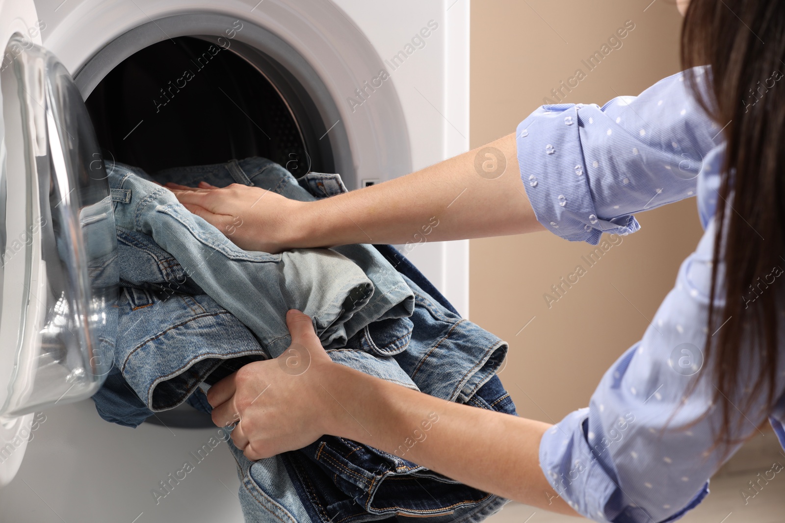 Photo of Woman putting dirty jeans and other denim clothes into washing machine, closeup