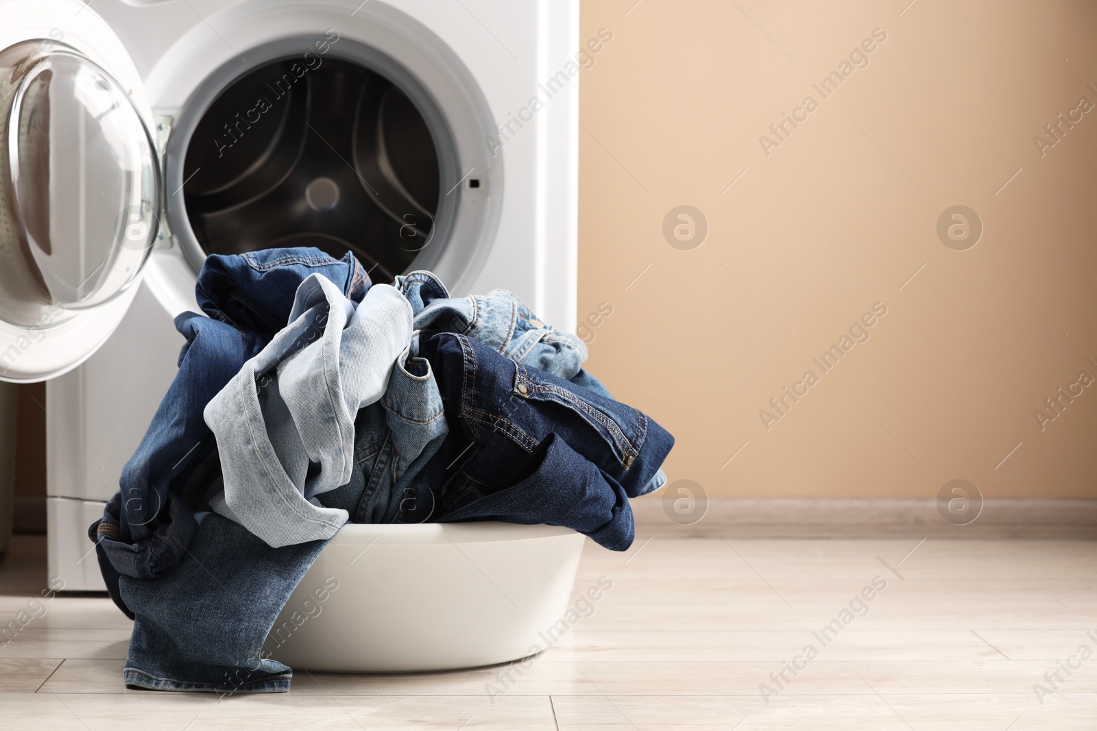 Photo of Washing machine with dirty jeans and other denim clothes indoors, space for text