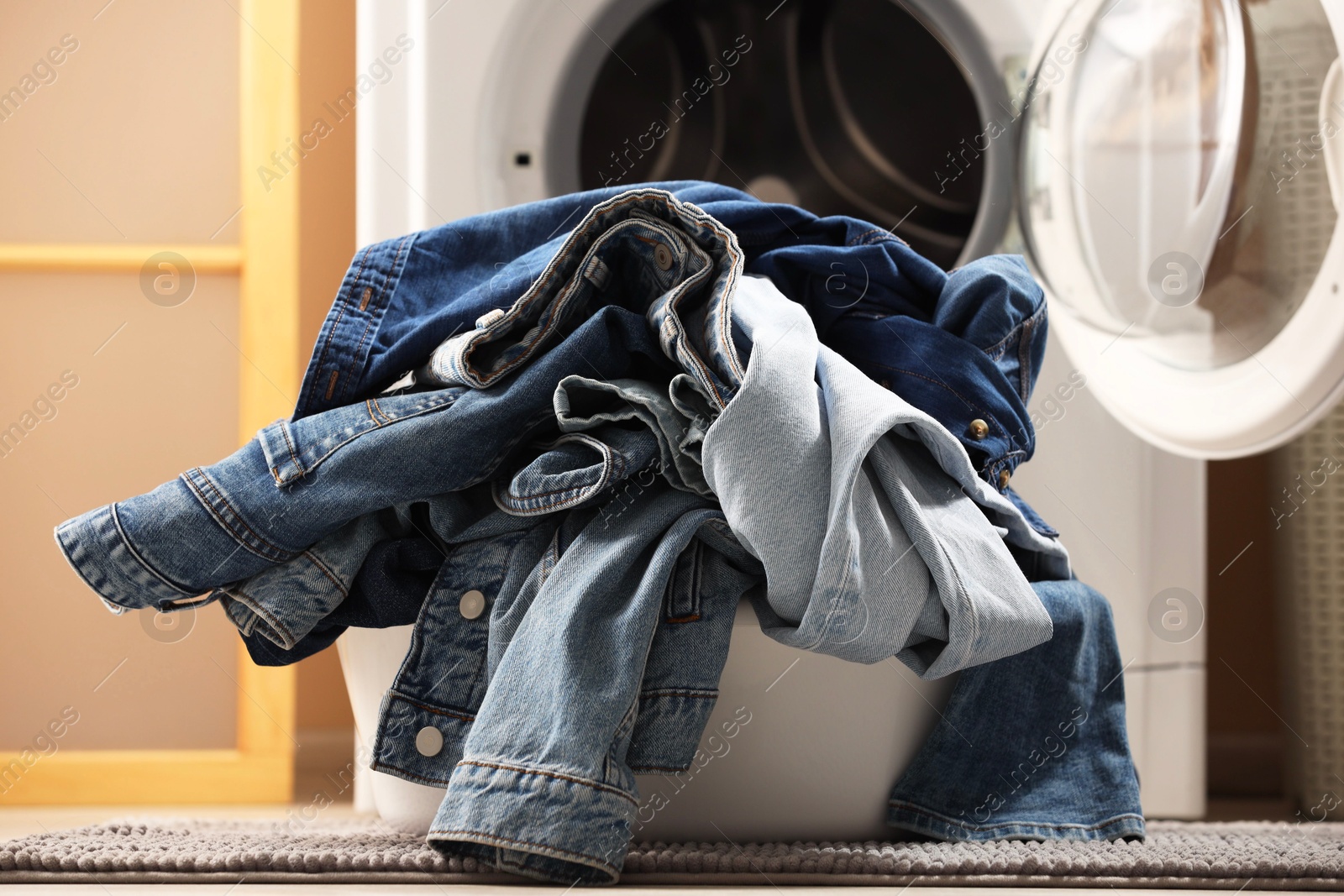 Photo of Washing machine with dirty jeans and other denim clothes indoors