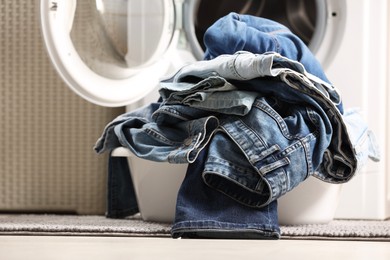 Photo of Washing machine with dirty jeans and other denim clothes indoors