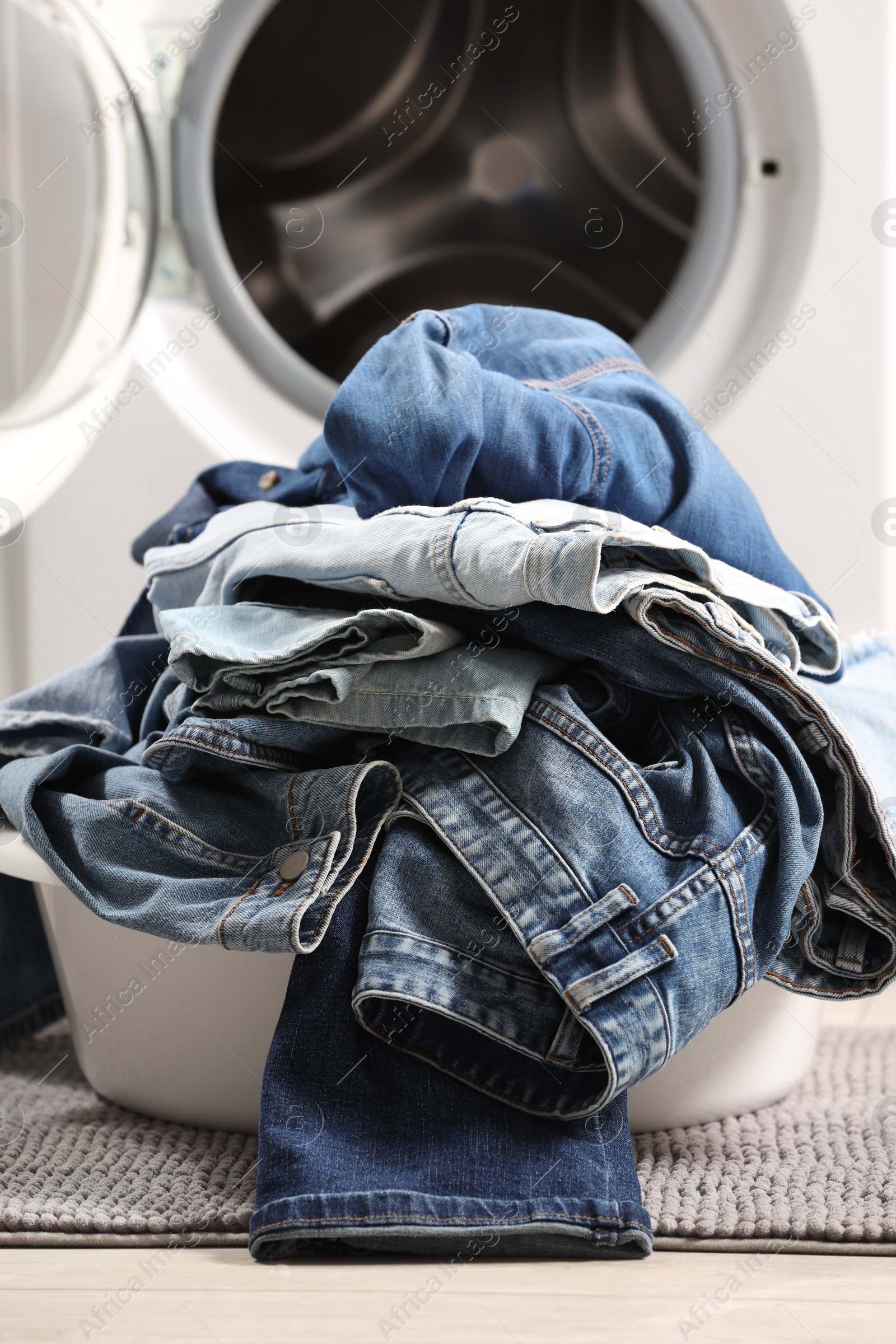 Photo of Washing machine with dirty jeans and other denim clothes indoors