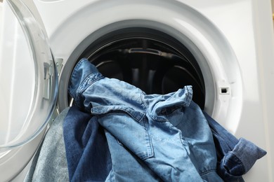 Washing machine with dirty jeans and other denim clothes indoors, closeup