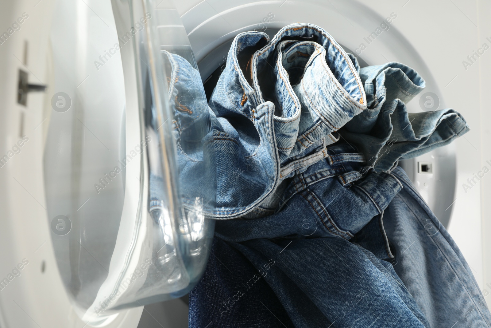 Photo of Washing machine with dirty jeans and other denim clothes indoors, closeup