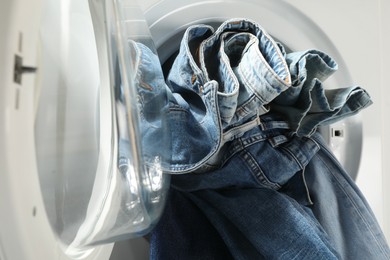 Photo of Washing machine with dirty jeans and other denim clothes indoors, closeup