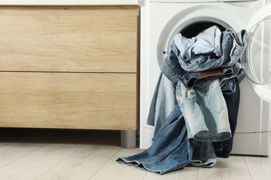 Photo of Washing machine with dirty jeans and other denim clothes indoors, space for text