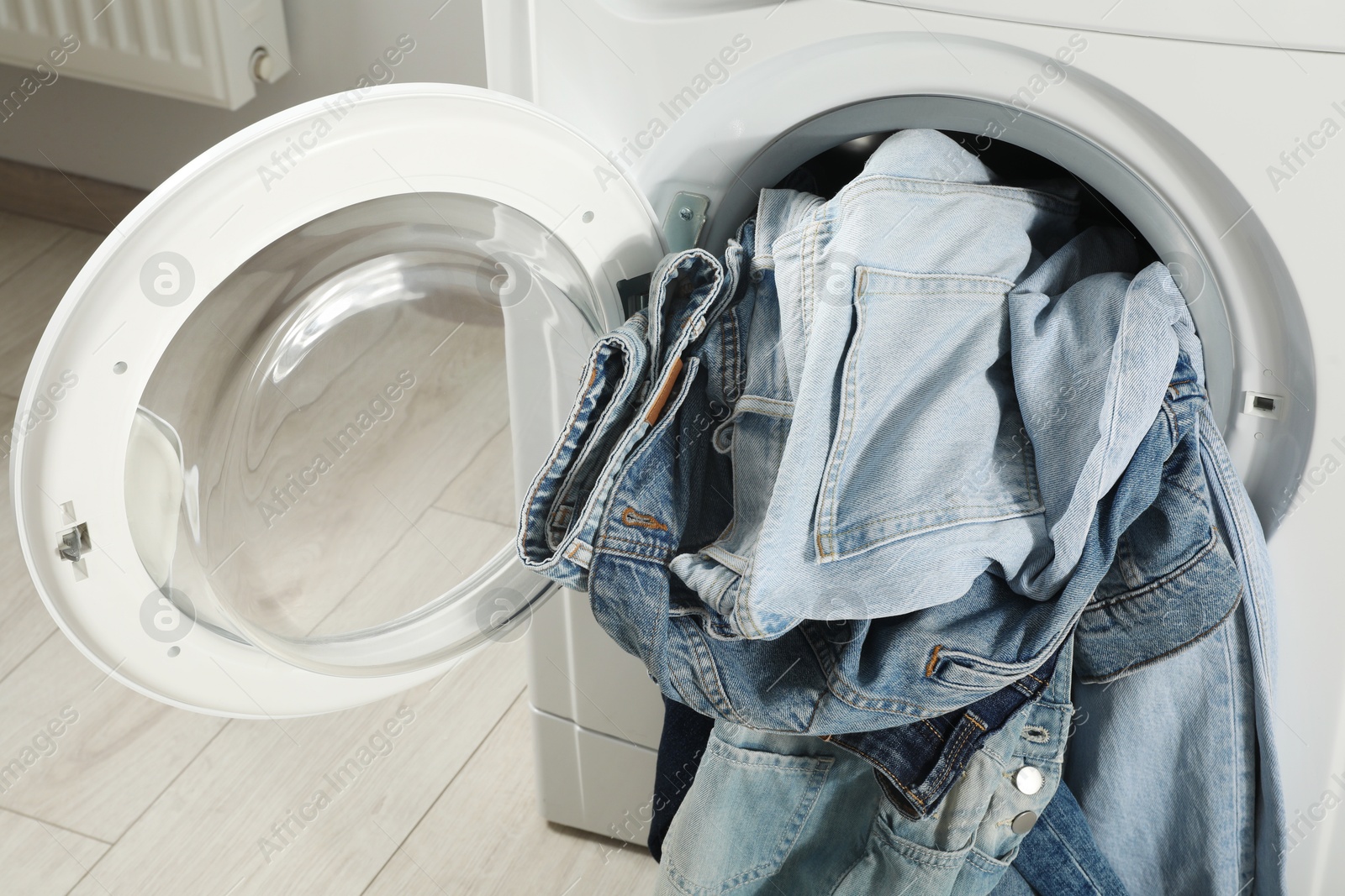 Photo of Washing machine with dirty jeans and other denim clothes indoors, closeup