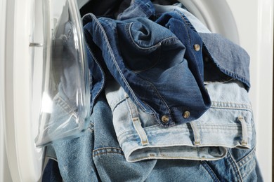 Photo of Washing machine with dirty jeans and other denim clothes indoors, closeup