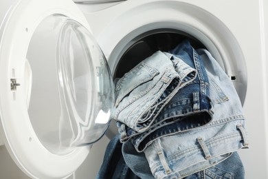 Photo of Washing machine with dirty jeans and other denim clothes indoors, closeup