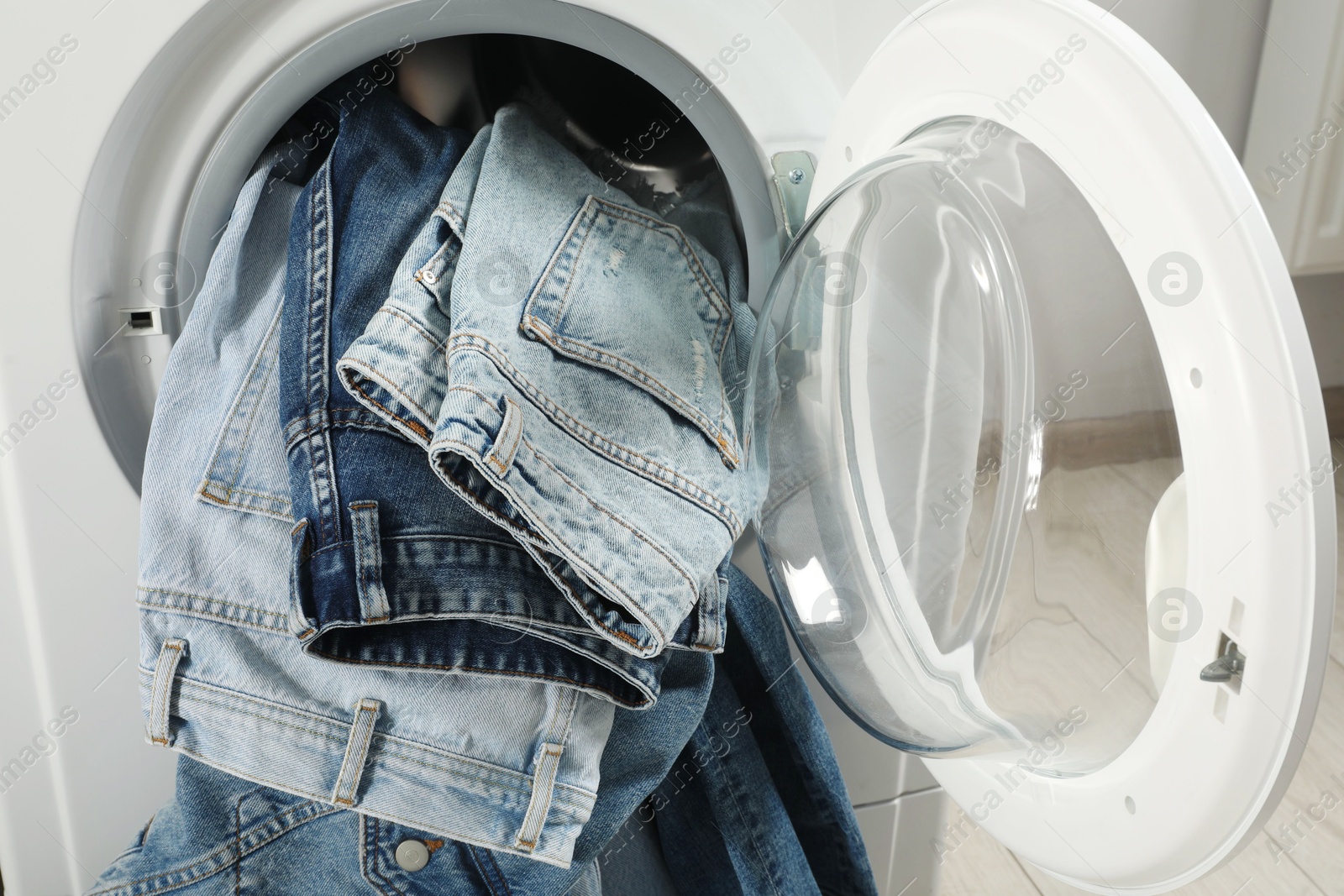 Photo of Washing machine with dirty jeans and other denim clothes indoors, closeup