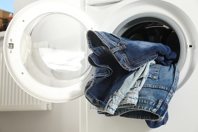 Photo of Washing machine with dirty jeans and other denim clothes indoors, closeup