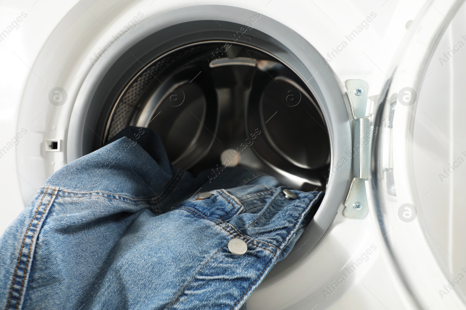 Photo of Washing machine with dirty denim jacket indoors, closeup