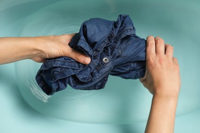 Photo of Woman washing denim clothes in basin, top view