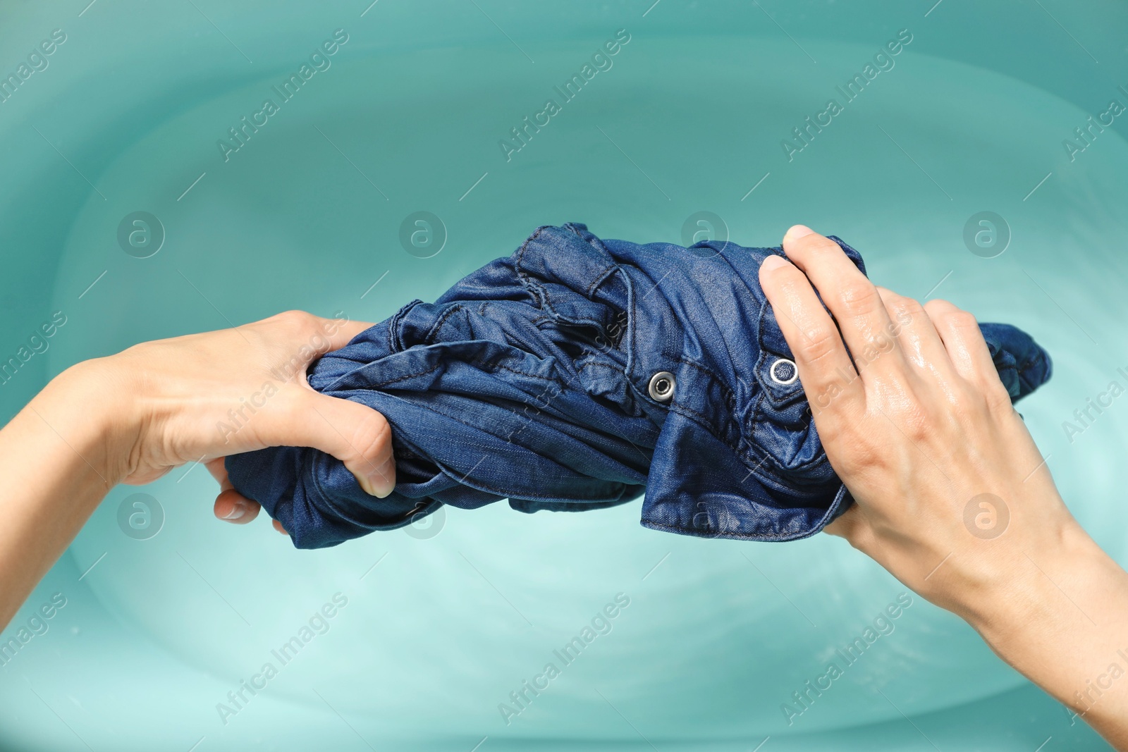 Photo of Woman washing denim clothes in basin, top view